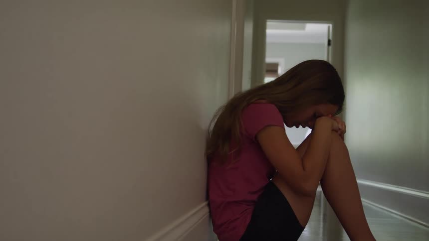 Young teenager sits on the hallway floor with her head on her knees
