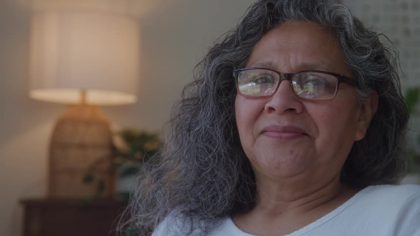 Older woman sitting indoors turns her head and smiles