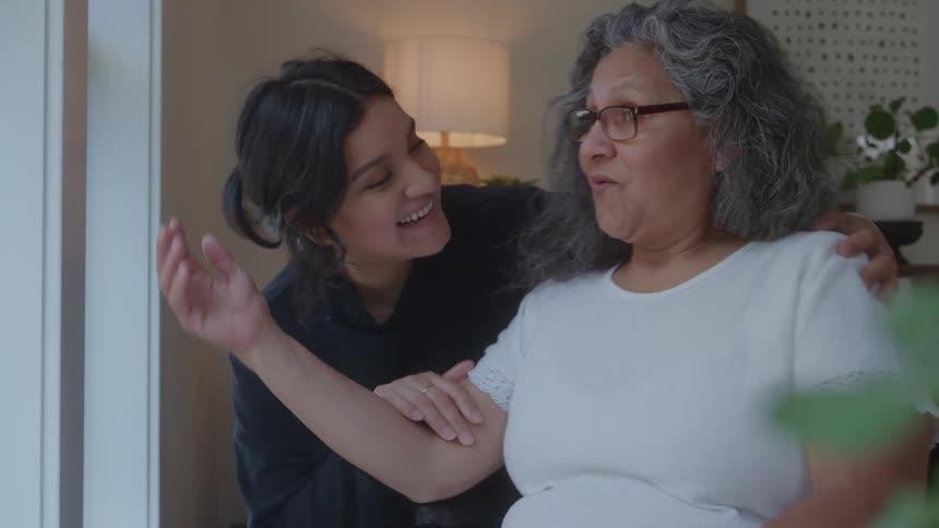 Mother and daughter hug affectionately by the window at home