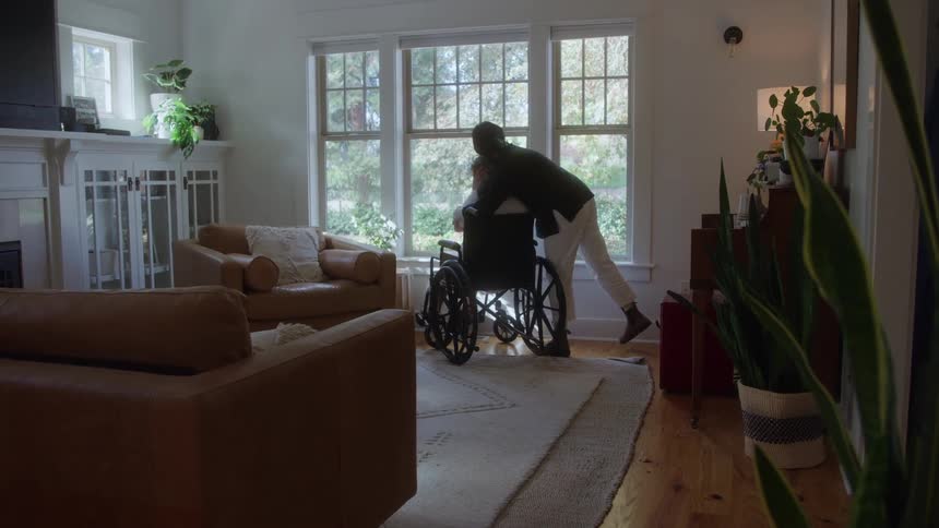Daughter embracing her mother in a wheelchair in a sunlit living room