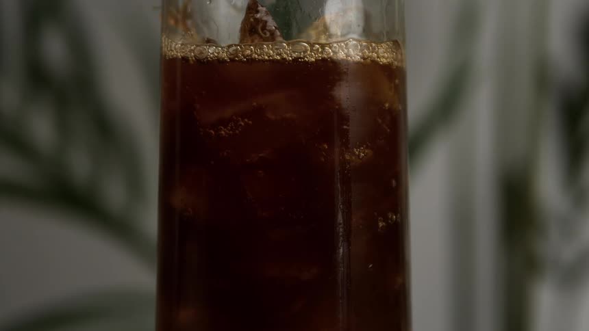 A dark soda is being poured on ice in a tall glass