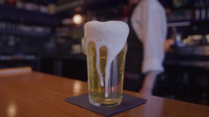 A bartender tops off a beer in a glass on the bar