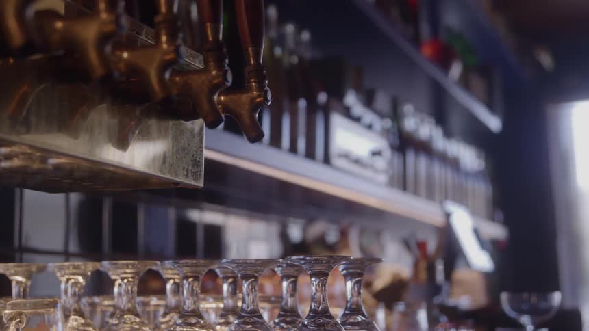 Upside down glassware stands on a counter next to the liquor dispensers in a bar