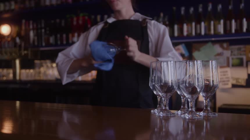 Female bartender wipes glassware while standing behind the bar
