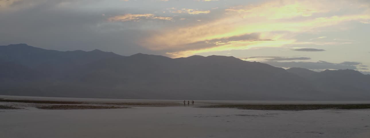 People are traveling on the sand ahead at dawn