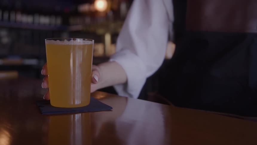 Female bartender places a beer on a napkin on the bar