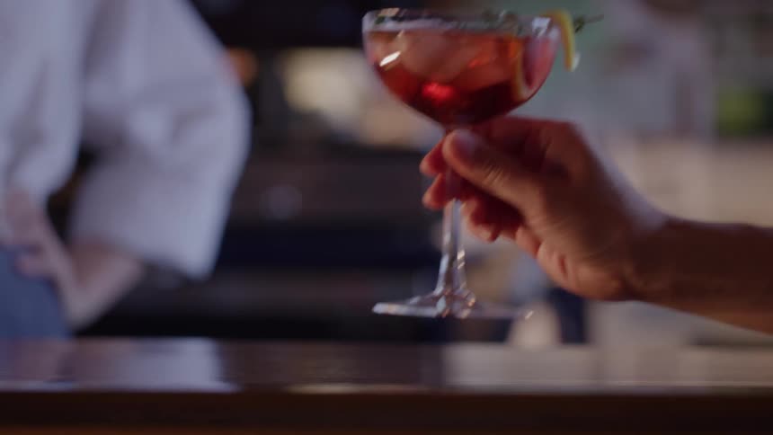 Customer picks up a cocktail from the bar while a bartender stands nearby