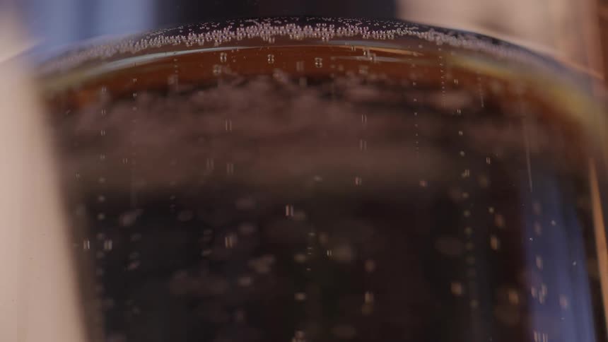 Close up of bubbles from a dark lager rising to rim of glass