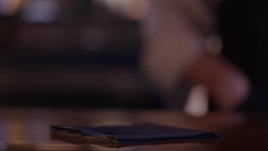 A persons hand taking an alcoholic drink from a black cloth with a slice of lemon on the side