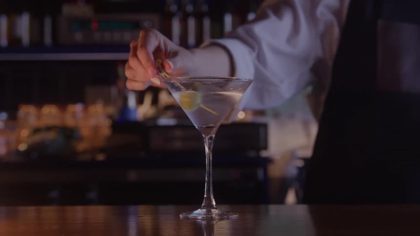 Female bartender adds an olive to a martini sitting on the bar