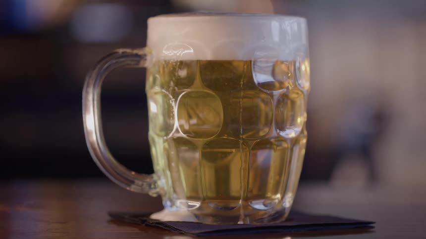 A mug of beer with a foam head is sitting on a napkin on a bar counter