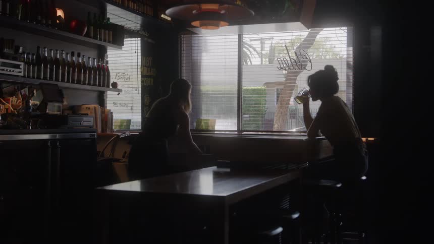A female sits at a dimly lit bar drinking while chatting with the female bartender