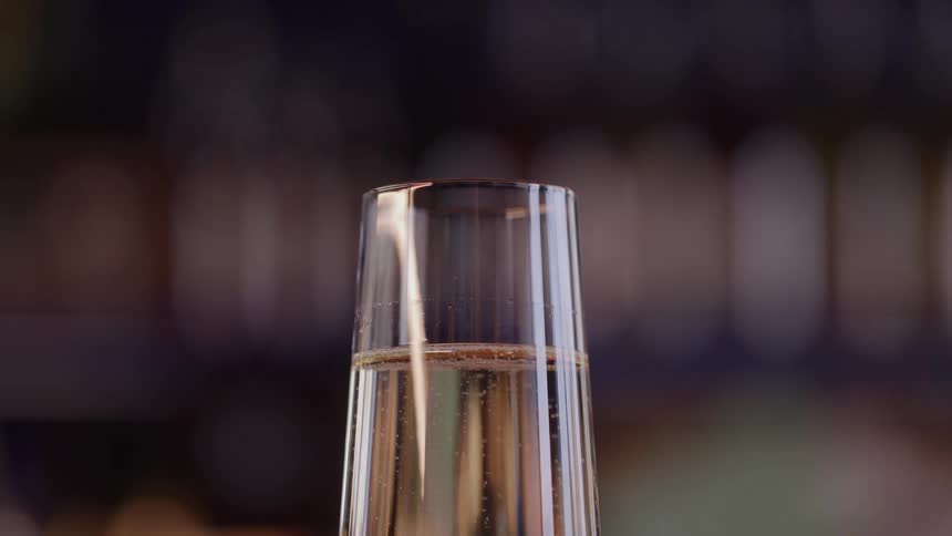 Tiny bubbles stream upwards through sparkling liquid in a glass flute set against a dark background with soft outoffocus lights