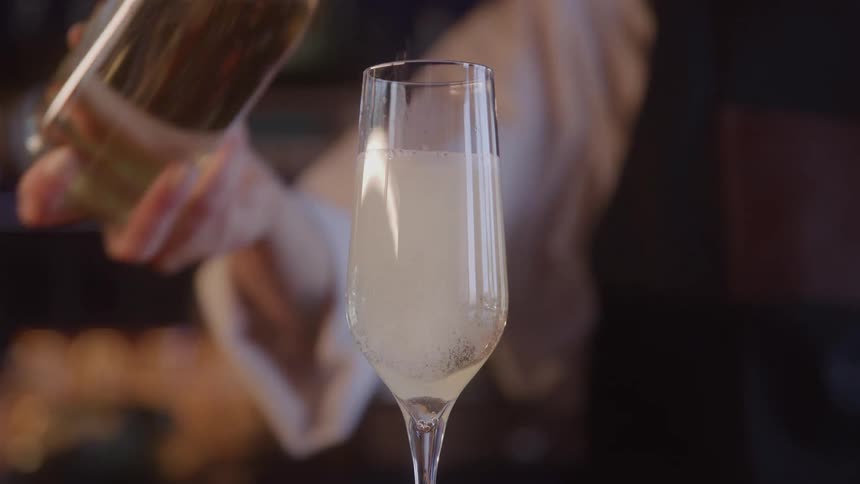 Bartender pours champagne into a long stemmed glass