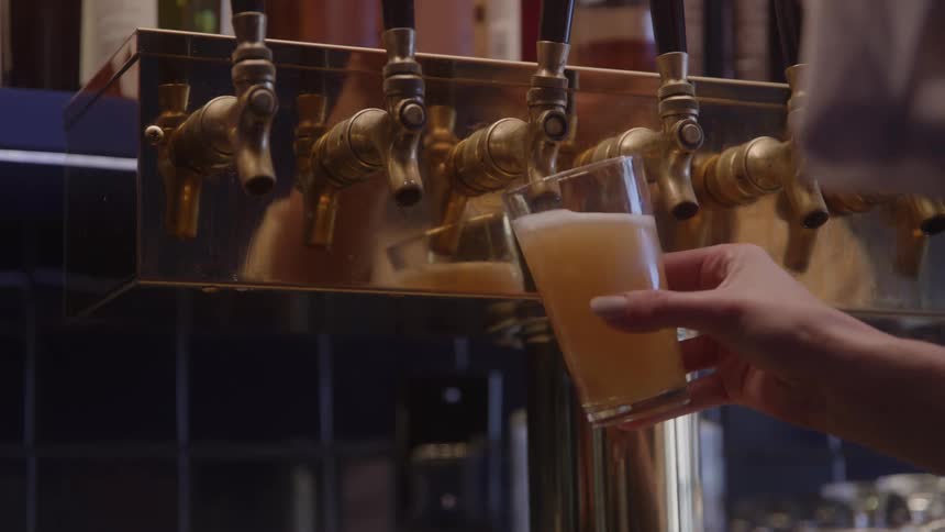 A female bartender pours beer from the tap in a beer glass