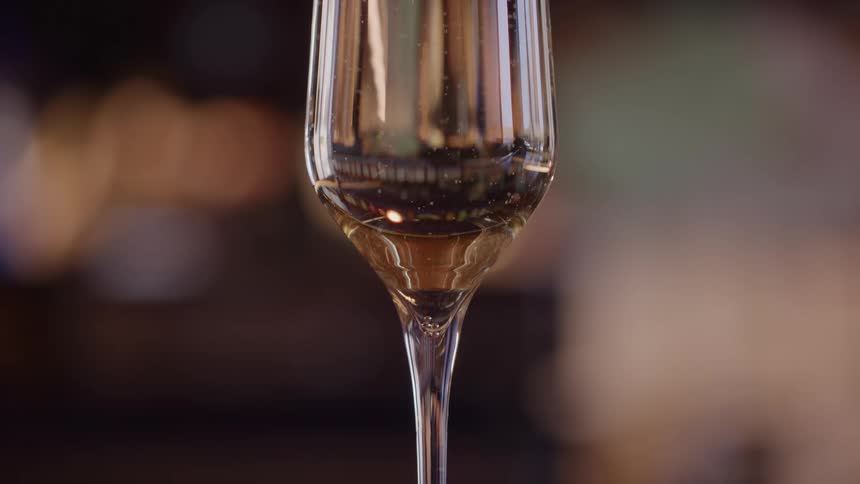 A very tight closeup shot focuses on the stem and lower bowl of a champagne flute the glass contains a pale golden liquid with tiny visible bubbles carbonation