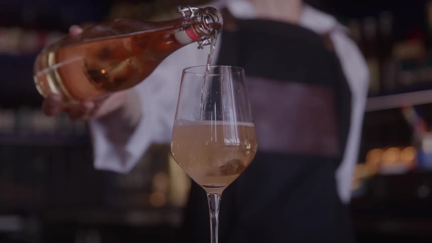 A bartender is pouring a glass of wine in a bar