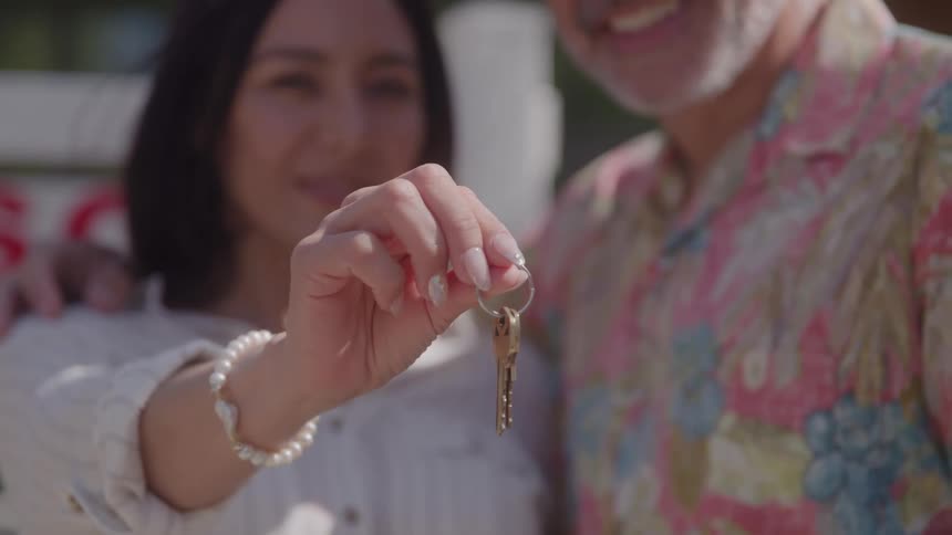 A smiling couple stands arm in arm as the woman holds a shiny house key