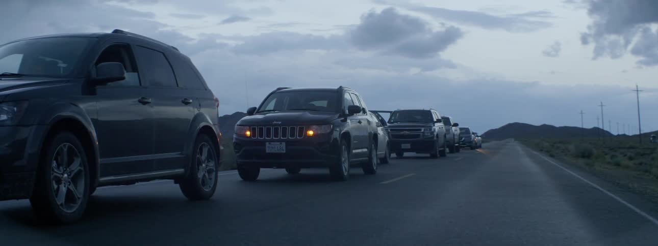 Cars are lined up on a rural road with the lights flashing on a jeep