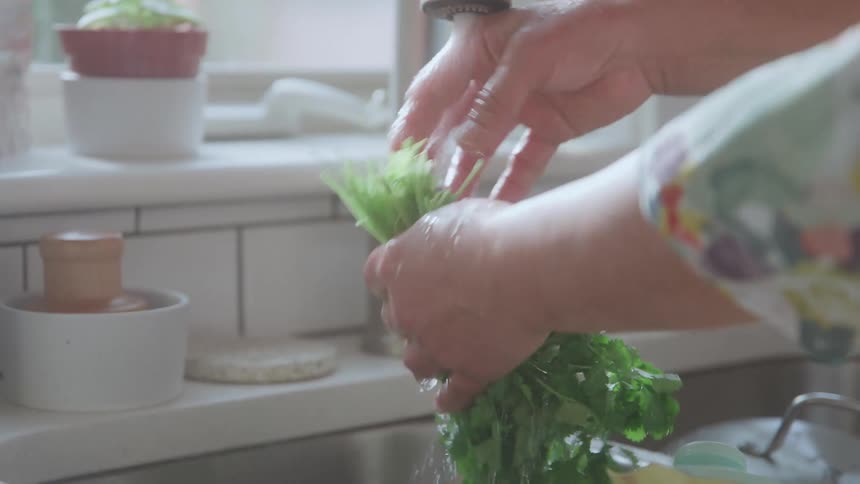A pair of hands rinses fresh greens under a running kitchen faucet