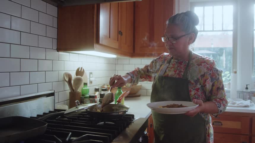 Woman plating food from a frying pan in a bright kitchen