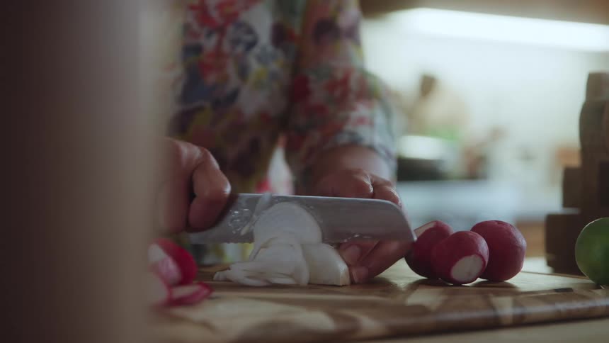 A woman is slicing radishes on a cutting board in a kitchen