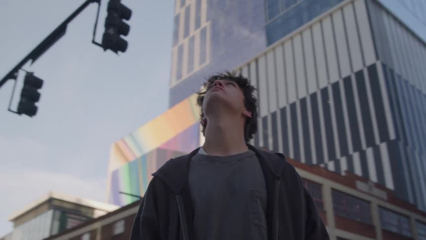 Young man stands at a downtown intersection and looks around at the buildings