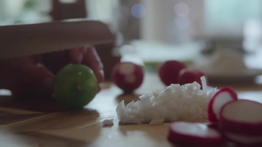 The video is a closeup shot of a persons hands chopping a white vegetable likely an onion into small pieces on a wooden cutting boardto the right there are slices of red radish near the diced vegetable suggesting the preparation of a colo
