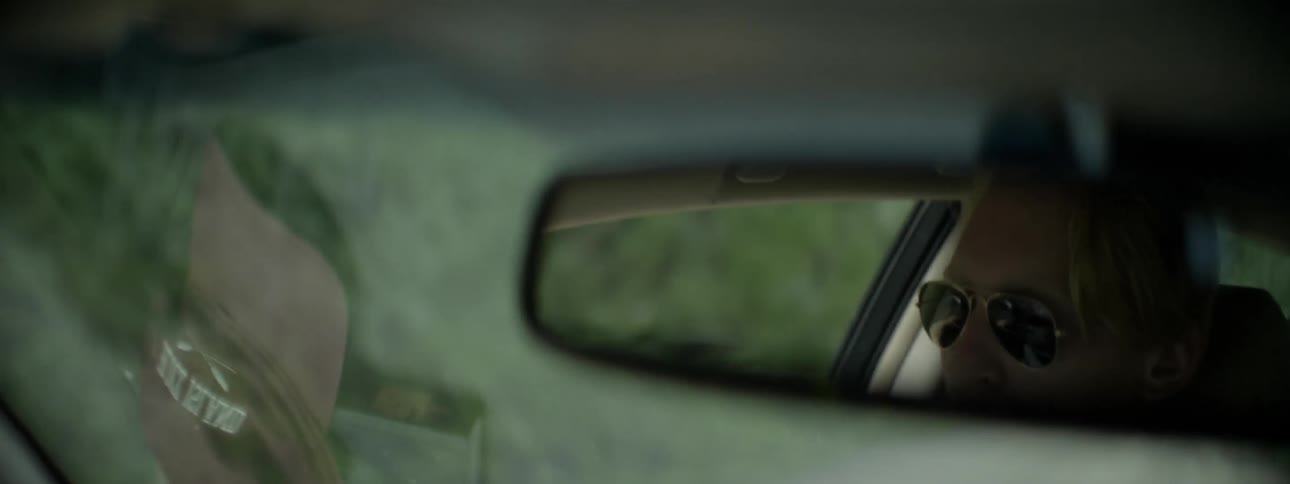 A man's face can be seen in the rear view mirror as he drives