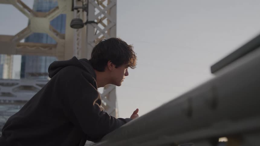 Young man leans on the railing of a bridge on a sunny day in the city