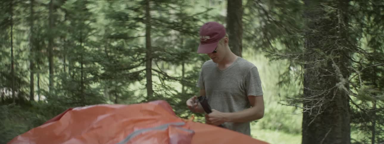 A man closes a small green bag while standing in the forest
