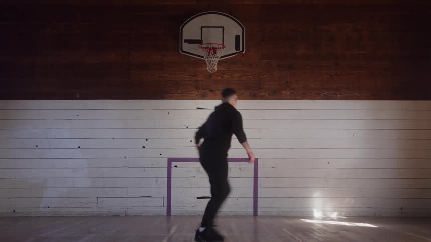 A person dribbles a basketball on a wooden court beneath a centered hoop