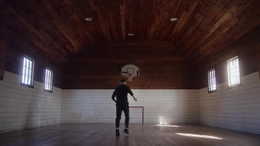 A young man is shooting hoops on the basketball court in a gym