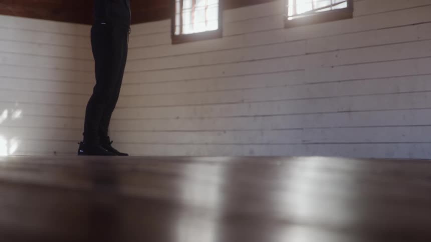 Person dribbles a basketball on an indoor court lit by sunlight
