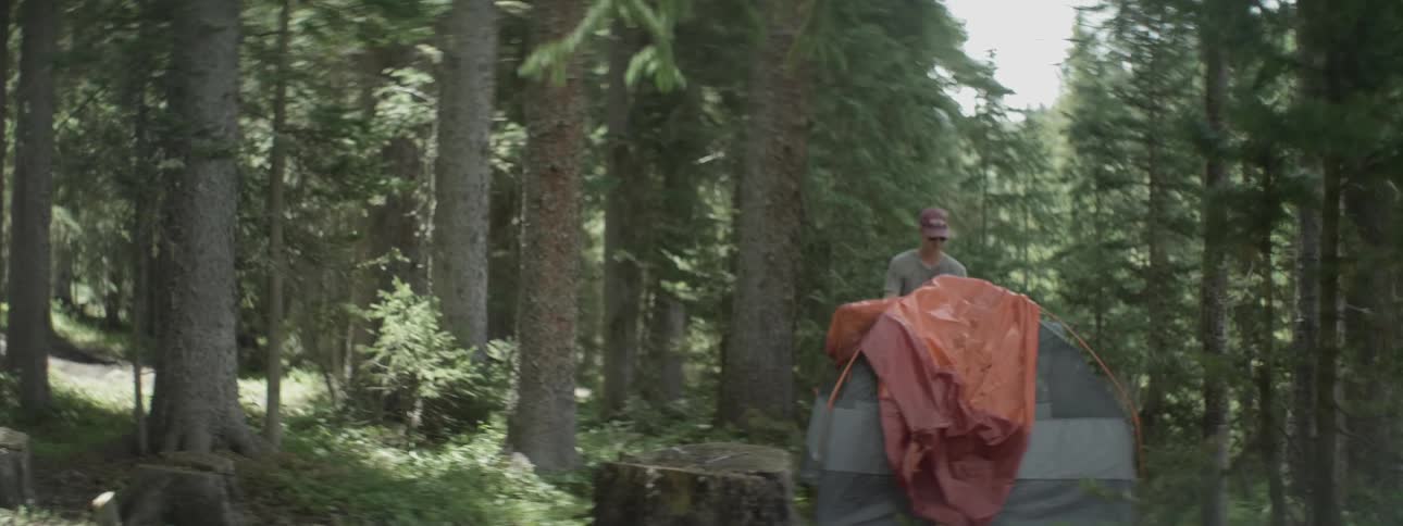 A man sets up a tent in the woods