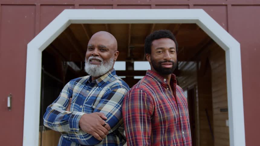 Father and son stand near the entrance to a farm building during the daytime