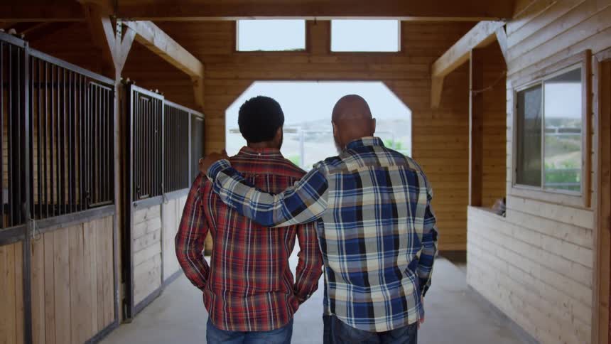 Father stands with an arm around his son in the stables during the daytime
