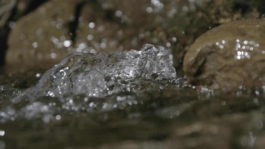 Close up of a clear water stream flowing between rocks outdoors during daytime
