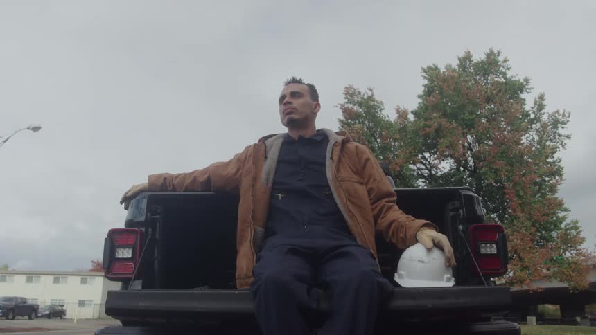 Male worker sits on the tailgate of a truck and rests during an overcast autumn day