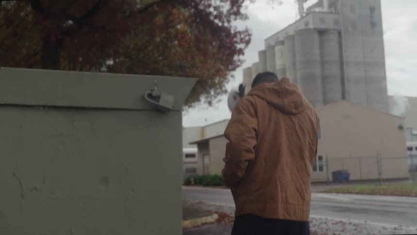 A worker walks alone near an industrial building on a cloudy day