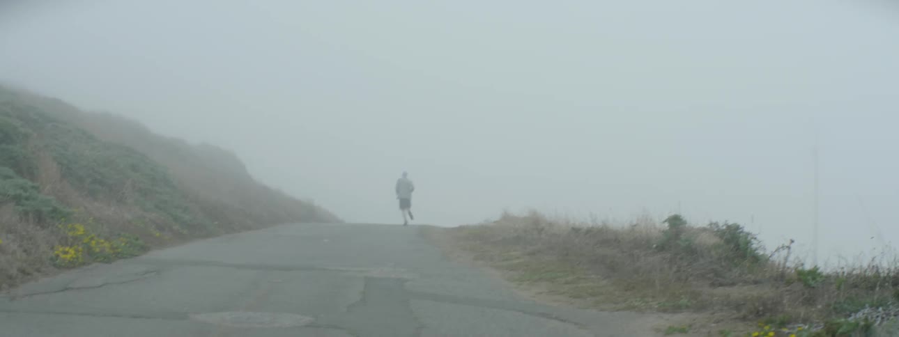 Man running down a road on a foggy day