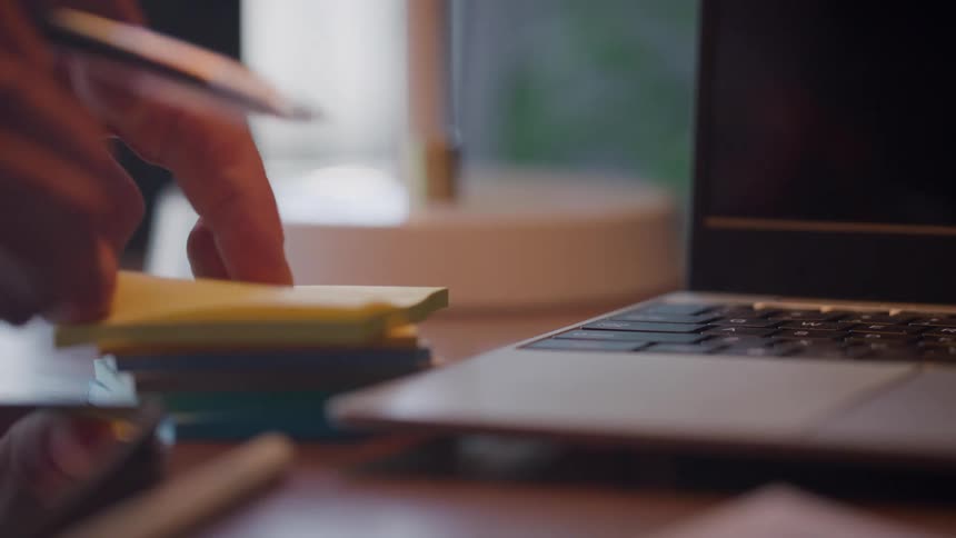 Close up of a person detaching a written sticky note on a work desk
