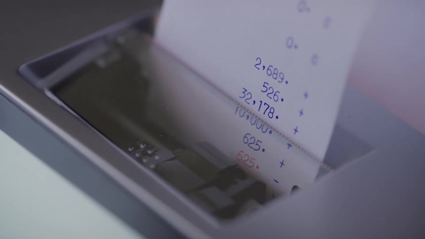 A printing calculator feeds a receipt tape with blue numbers and plus signs visible