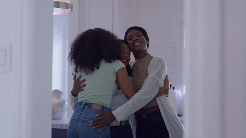 Mother and her two daughters share a group hug while standing in the kitchen during the daytime