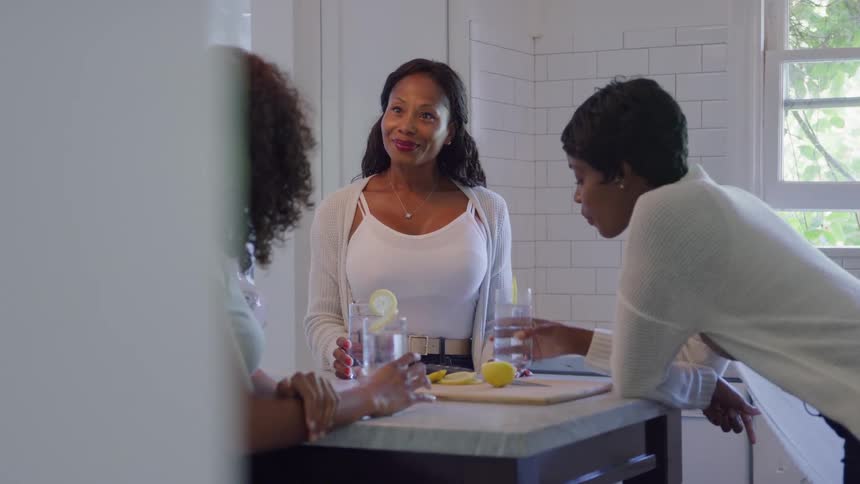 Three women enjoying drinks and talking in a bright kitchen