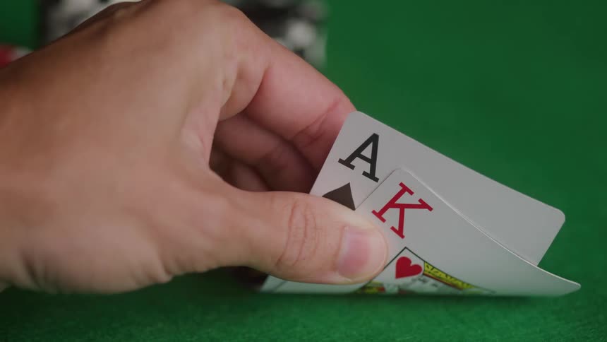 Hand holds ace of spades and king of hearts on green felt with blurred chips in background
