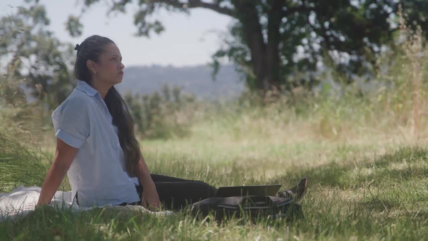A young woman sits alone on the grass at midday