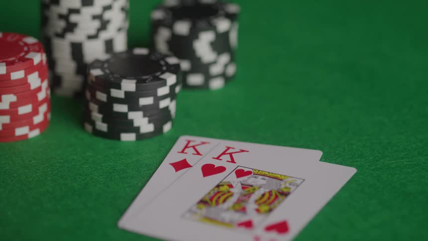 A person drops a pair of king playing cards next to a stack of poker chips