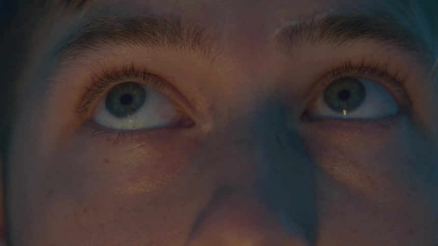 The video is an extreme closeup focusing on a persons eyes and the immediate surrounding skinthe lighting is dramatic with one side of the face lit by an unnatural blue light that creates a strong color contrast