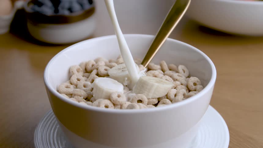 Pouring milk over cereal and bananas in a white bowl